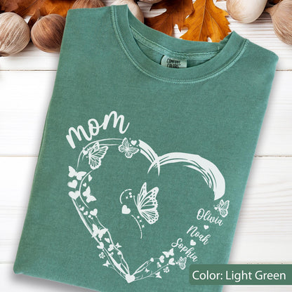 May include: Light green t-shirt with a white heart-shaped design filled with butterflies and the word "mom". The names Olivia, Noah, and Sophia are printed on the heart. The shirt is a Comfort Colors brand.