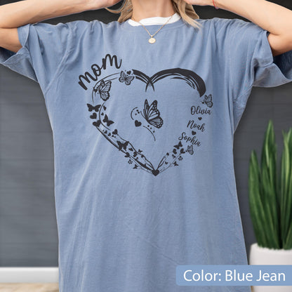 May include: Blue jean colored t-shirt with a heart-shaped design. The design includes the word "mom" in cursive, butterflies, and the names Olivia, Noah, and Sophia. The shirt is a comfortable, casual style.