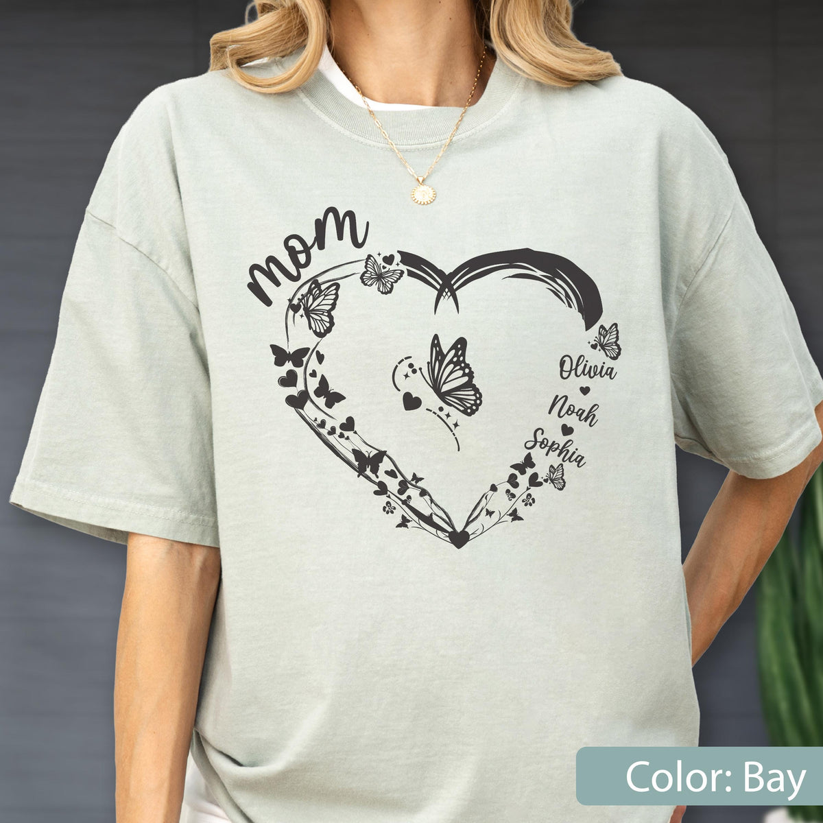 May include: A light green t-shirt with a heart-shaped design filled with butterflies and the word "mom" at the top. The names Olivia, Noah, and Sophia are listed inside the heart. The shirt is a bay color.