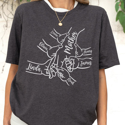May include: Dark gray t-shirt featuring a white graphic of hands clasped together, with the word "Mother" and names like Emma, Olivia, Linda, Henry, James, and Noah. The shirt has a round neckline and short sleeves.