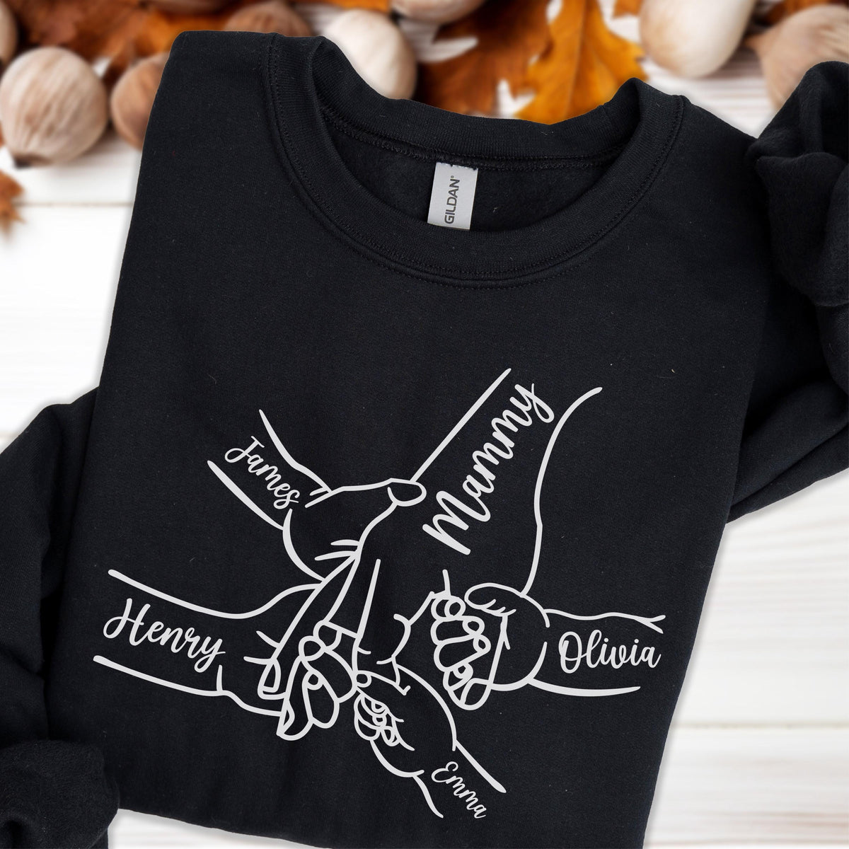 May include: Black sweatshirt with a white graphic of hands holding each other, with the names "James", "Mammy", "Henry", "Olivia", and "Emma" printed on the design. The sweatshirt is made of a soft material.