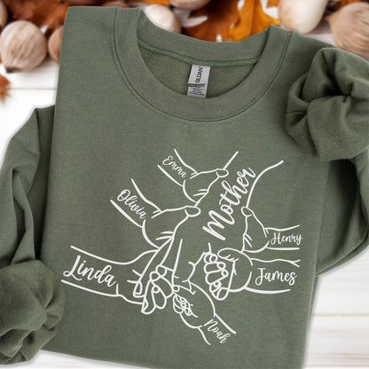 May include: An olive green sweatshirt with the word "Mother" in the center, surrounded by hands with names like "Emma", "Olivia", "Linda", "Henry", "James", and "Noah". The sweatshirt has a crew neck and long sleeves.