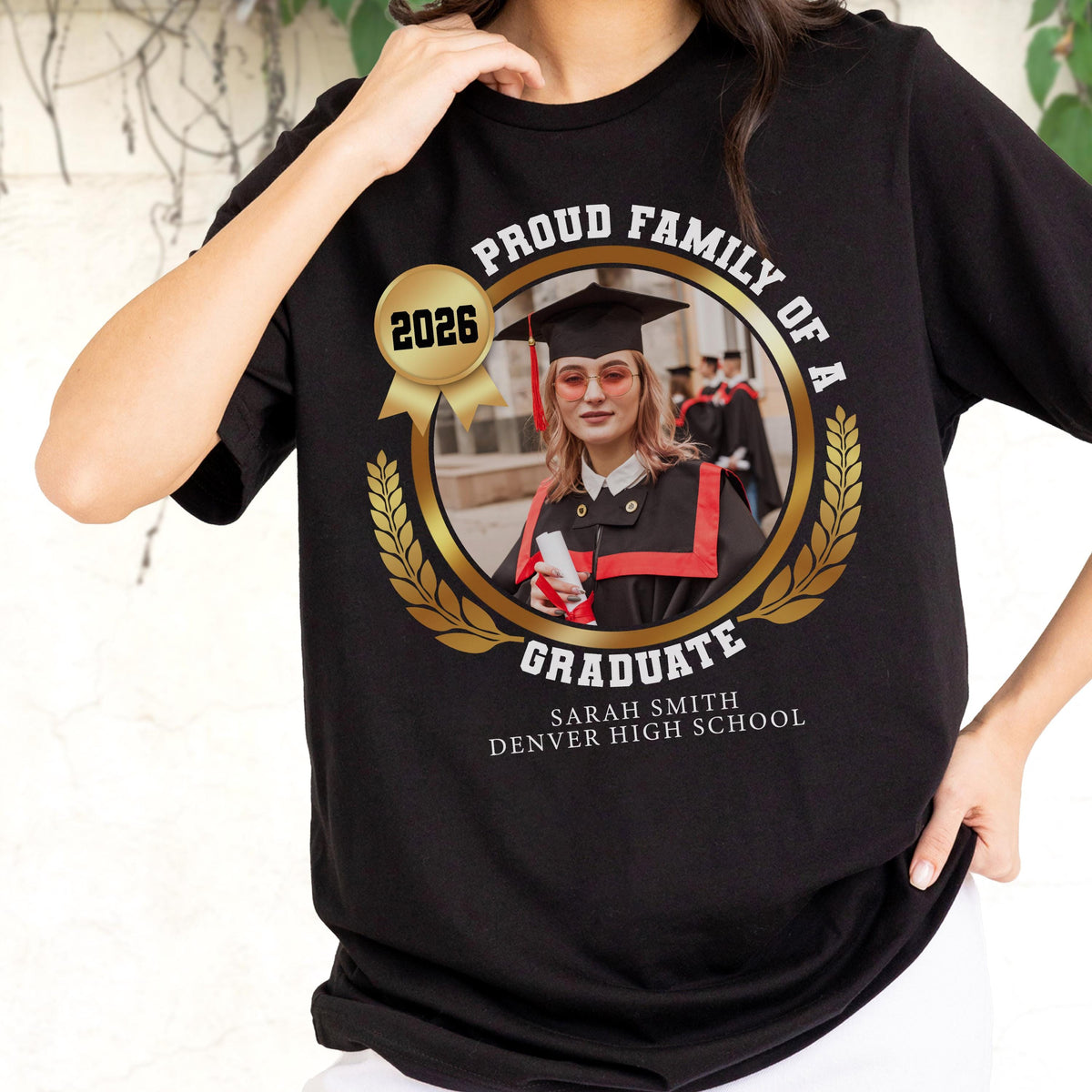 May include: Black t-shirt with a gold circular design featuring a graduate in a cap and gown. The design includes the text "PROUD FAMILY OF A GRADUATE" and "2026". The graduate's name and high school are also printed on the shirt.