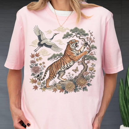 May include: Pink t-shirt featuring a detailed illustration of a tiger, crane, and floral elements. The tiger is depicted climbing a tree, with a crane flying in the background. The design includes various flowers and clouds.