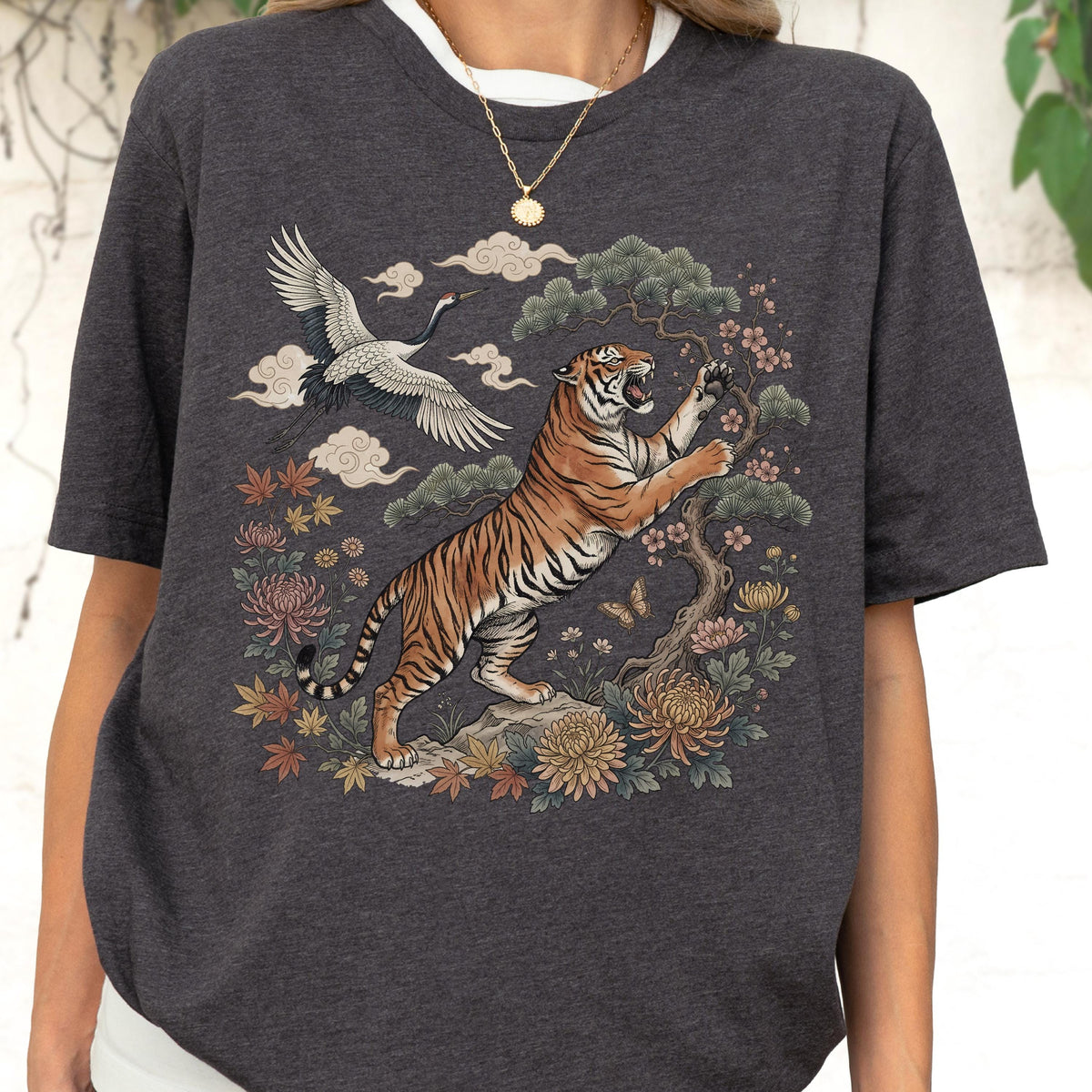 May include: Dark gray t-shirt featuring a detailed illustration of a tiger, crane, and floral elements. The tiger is orange and black, set against a backdrop of clouds and flowers. The design has an Asian-inspired aesthetic.