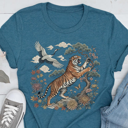 May include: Teal t-shirt featuring a detailed illustration of a tiger, crane, and floral elements. The tiger is orange and black, set against a backdrop of clouds, flowers, and a bonsai tree. A gray sneaker is visible in the lower left corner.