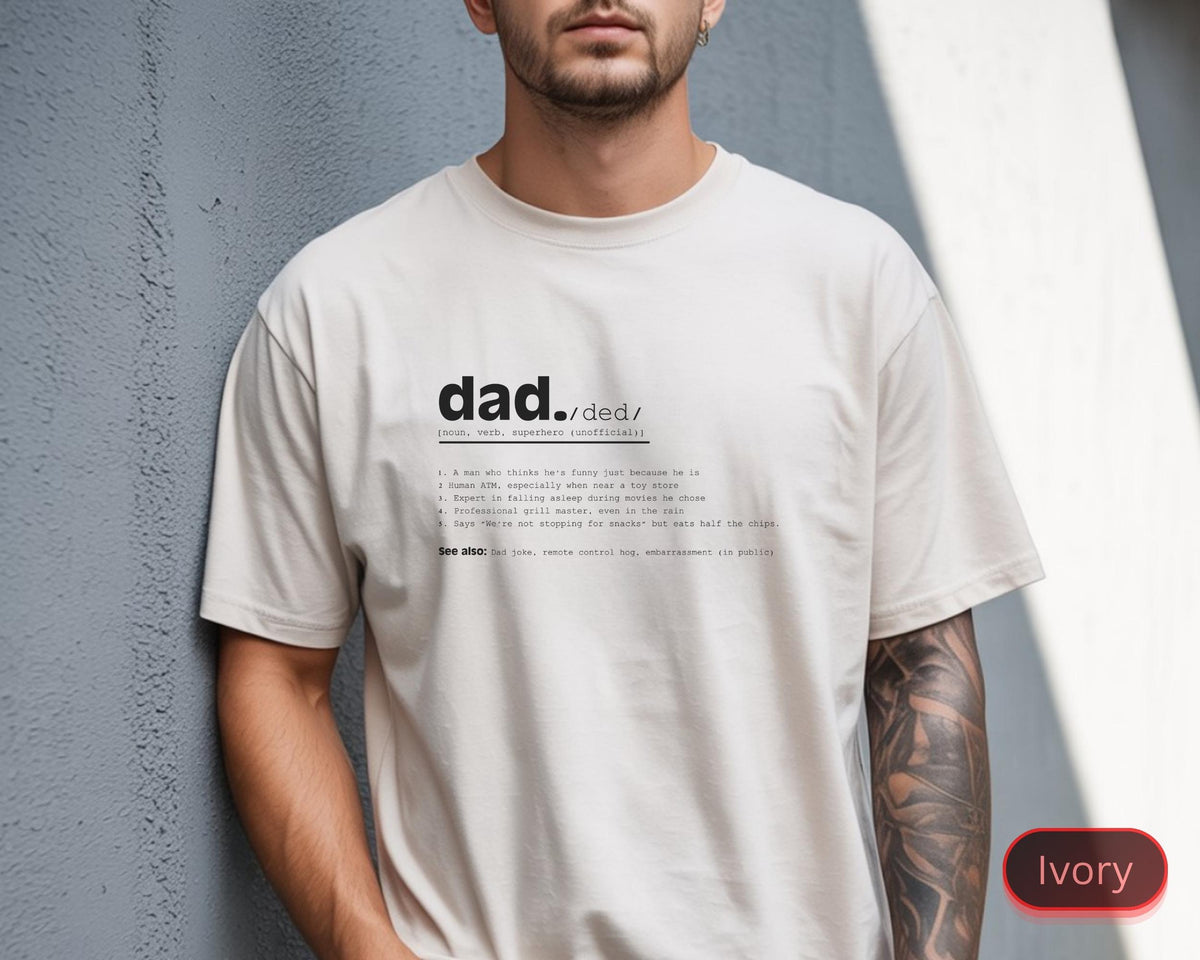 May include: Ivory-colored t-shirt with the word "dad" and its definition printed in black. The definition includes numbered points and the phrase "See also". The shirt is a relaxed fit.