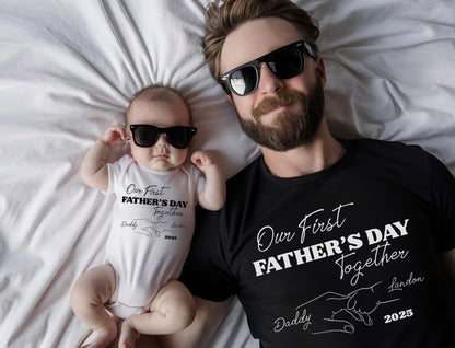 May include: A black t-shirt and a white baby onesie, both with the text "Our First Father's Day Together". The onesie and t-shirt also have a graphic of two hands holding each other. Both are wearing black sunglasses.