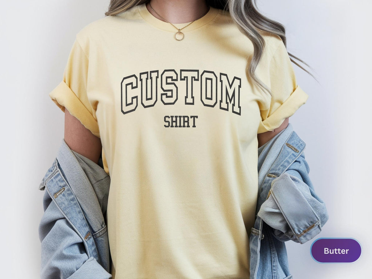May include: Butter yellow t-shirt with the word "CUSTOM" above "SHIRT" in a black, collegiate-style font. The shirt has rolled-up sleeves and is paired with a light blue denim jacket.