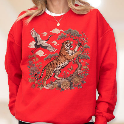 May include: Red sweatshirt featuring a detailed illustration of a tiger, crane, and floral elements. The tiger is depicted with orange and black stripes, reaching towards a tree. A crane flies in the background, with clouds and flowers completing the design.