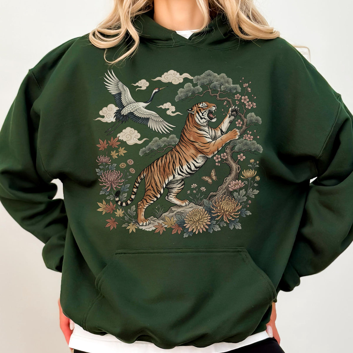 May include: Dark green hoodie featuring a detailed illustration of a tiger, crane, and floral elements. The tiger is depicted in a dynamic pose amidst a Japanese-inspired landscape. The design includes clouds, flowers, and a tree.