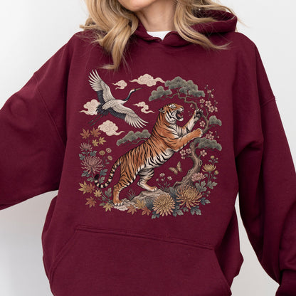 May include: Burgundy hoodie featuring a detailed illustration of a tiger, crane, and floral elements. The tiger is orange and black, set against a backdrop of clouds and flowers. The design has an Asian-inspired aesthetic, perfect for casual wear.