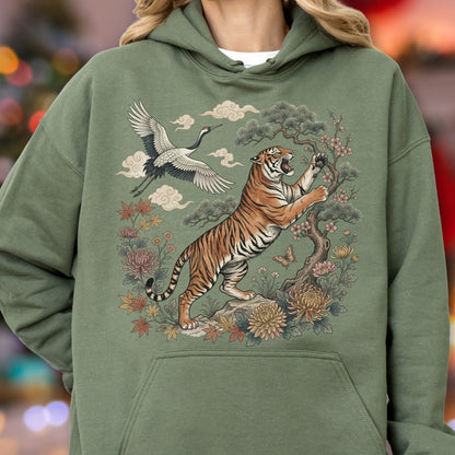 May include: Sage green hoodie featuring a detailed illustration of a tiger, crane, and floral elements. The tiger is depicted with orange and black stripes, reaching towards a tree. The design includes clouds and flowers, creating a nature-inspired theme.
