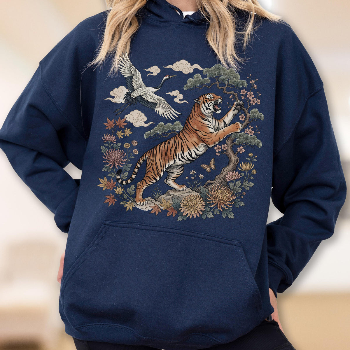 May include: Navy blue hoodie featuring a detailed illustration of a tiger, crane, and floral elements. The tiger is orange and black, set against a backdrop of clouds and flowers. The design is centered on the front of the hooded sweatshirt.