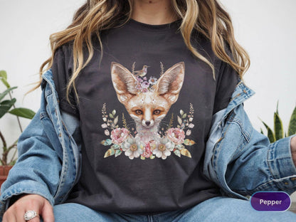 May include: Dark gray t-shirt featuring a watercolor illustration of a fennec fox with large ears, adorned with flowers and a small bird. The fox is surrounded by a floral wreath in pastel colors. The word "Pepper" is visible on the bottom right.