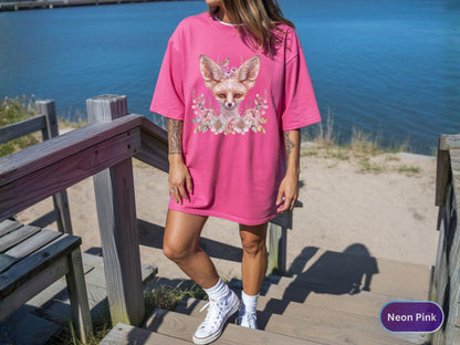 May include: Neon pink oversized t-shirt featuring a fox graphic with floral accents. The fox has a crown and is surrounded by flowers. The shirt is a vibrant pink color and has short sleeves.