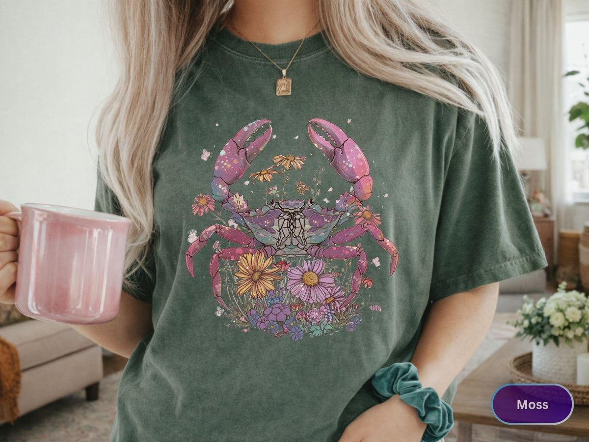 May include: Moss green t-shirt featuring a colorful crab design with flowers. The crab has pink claws and legs, with a purple body. The flowers are yellow, pink, and purple. The shirt is a relaxed fit.