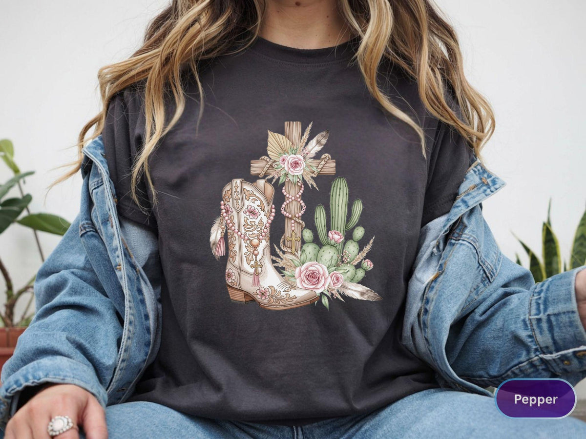 May include: Dark gray t-shirt featuring a Western-themed graphic. The design includes a cowboy boot, a cross, cacti, and flowers in soft, muted colors. The word "Pepper" is visible on the bottom right.