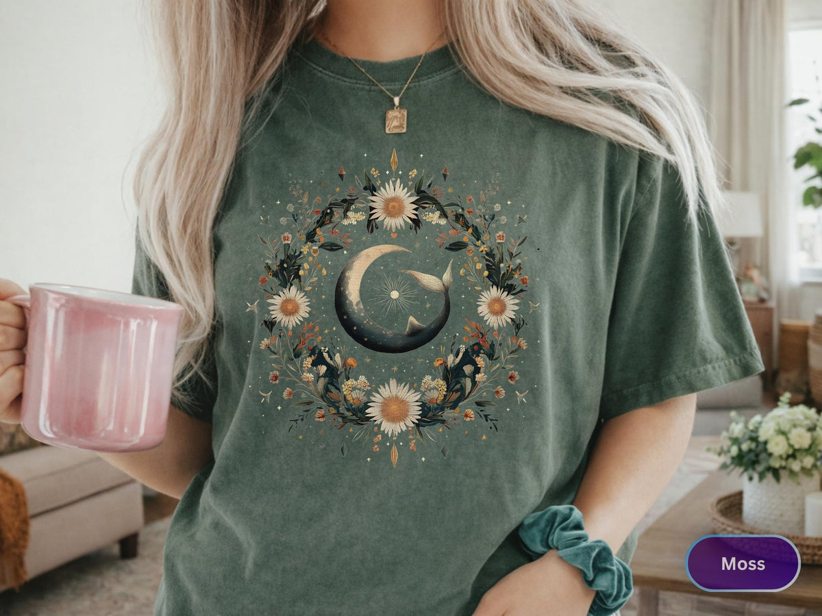 May include: Moss green t-shirt featuring a floral and celestial design. The graphic includes a crescent moon, a whale, and a wreath of flowers. The shirt is a comfortable, casual style.