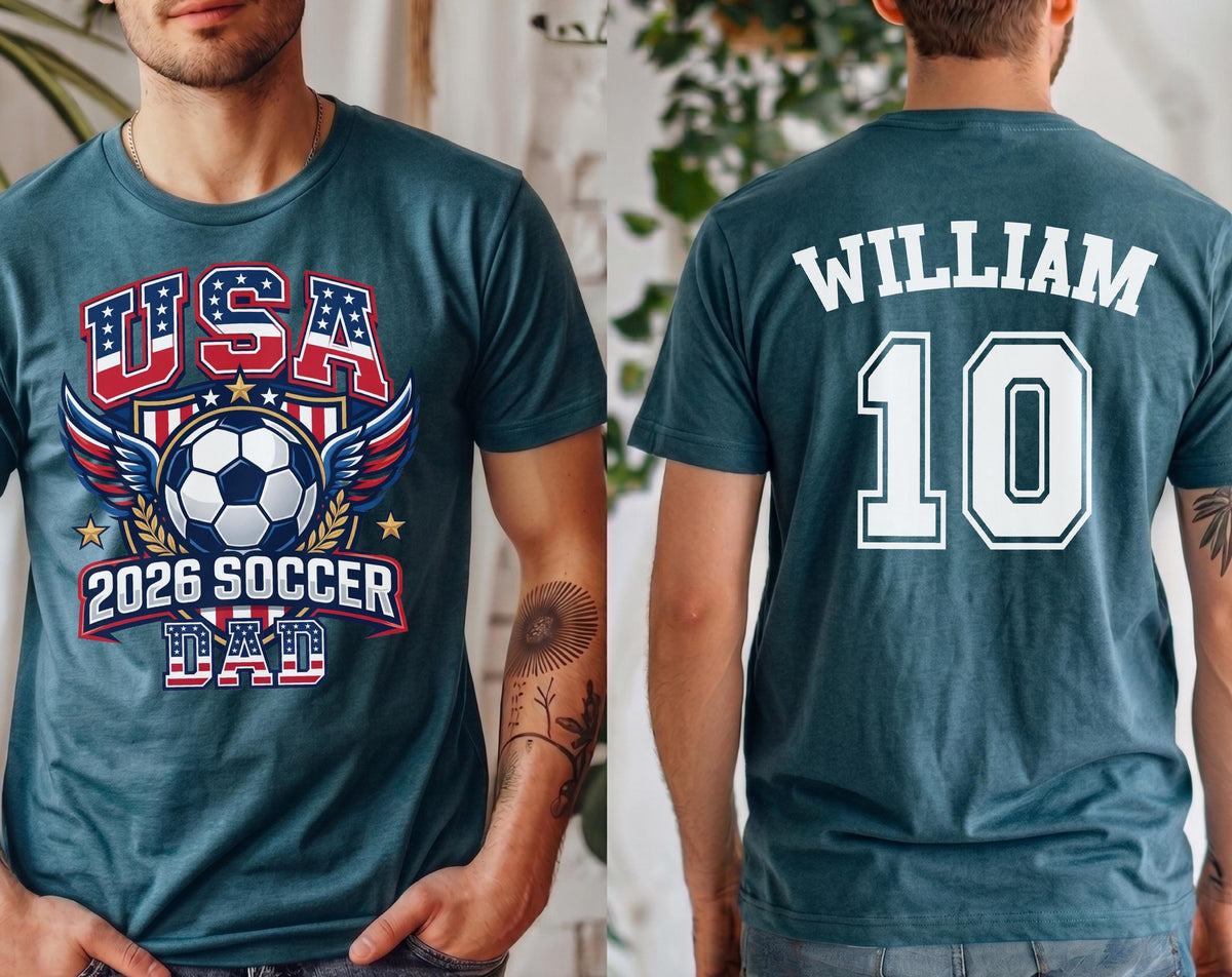 May include: Teal t-shirt with a soccer-themed graphic. The front features "USA" in red, white, and blue, a soccer ball, wings, and "2026 SOCCER DAD." The back displays "WILLIAM" and the number "10" in white.