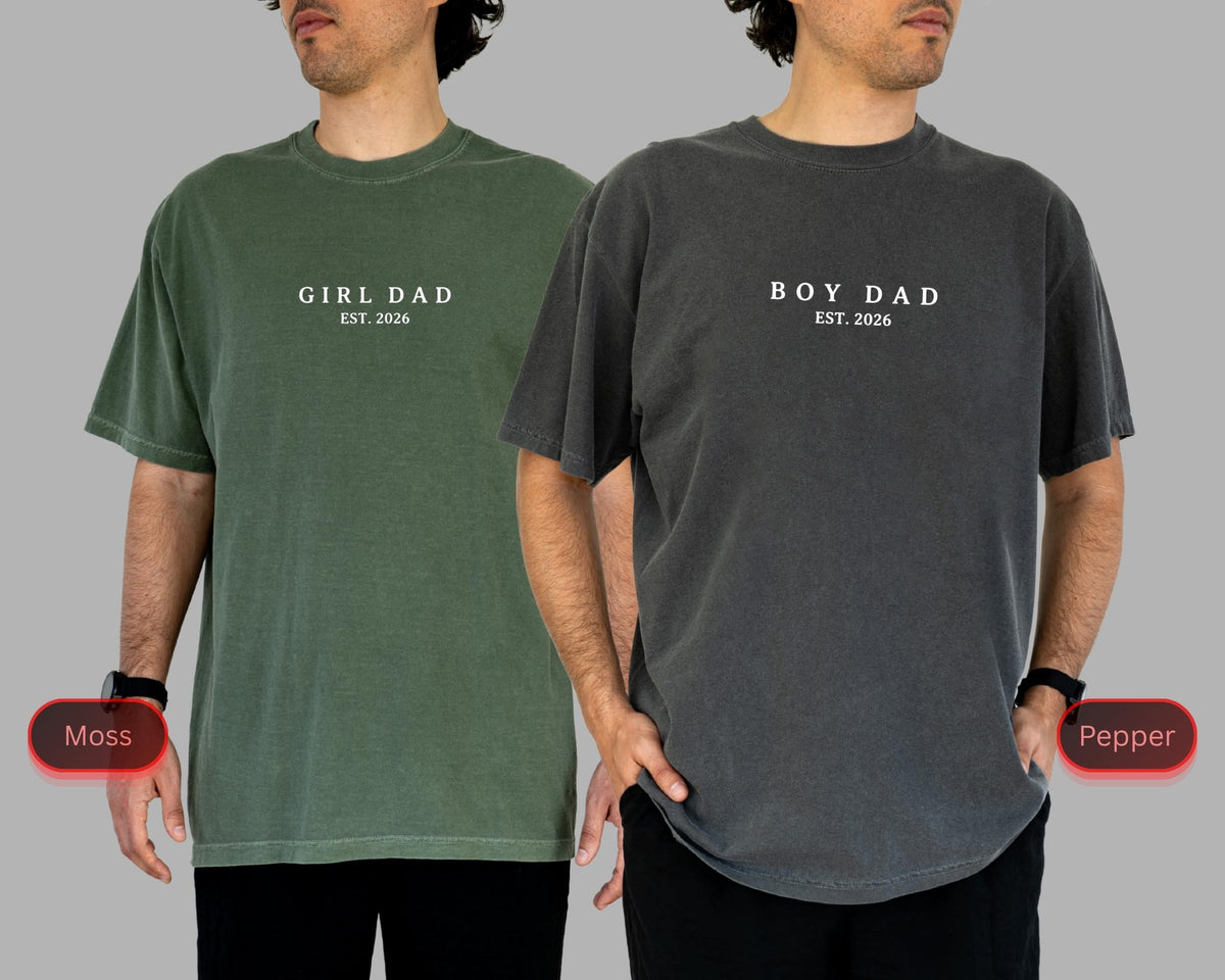 May include: Two short-sleeved t-shirts, one moss green and one pepper gray. The moss green shirt has the text "GIRL DAD EST. 2026" printed in white. The pepper gray shirt has the text "BOY DAD EST. 2026" printed in white.