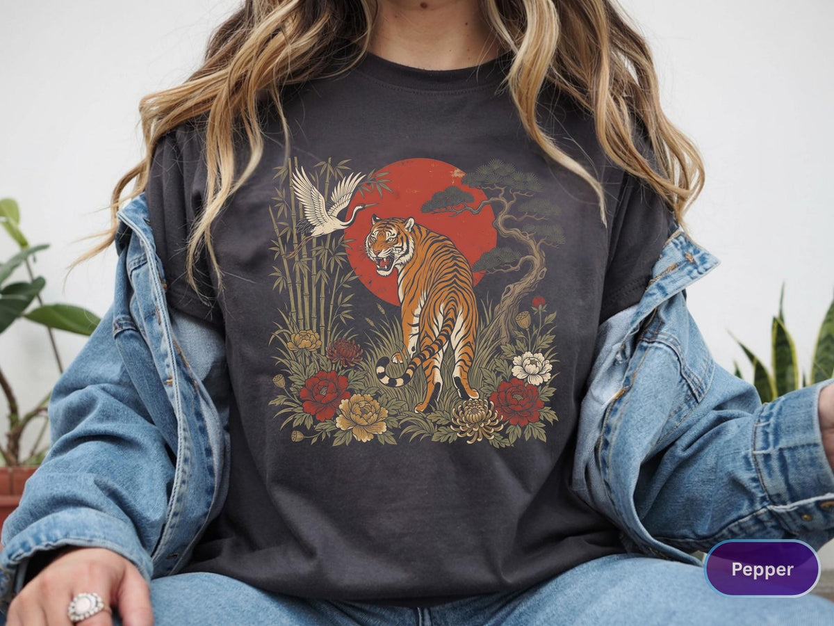 May include: Dark gray t-shirt featuring a tiger illustration with a red sun, crane, and floral elements. The design has an Asian-inspired aesthetic. The shirt is a comfortable, casual wear item.
