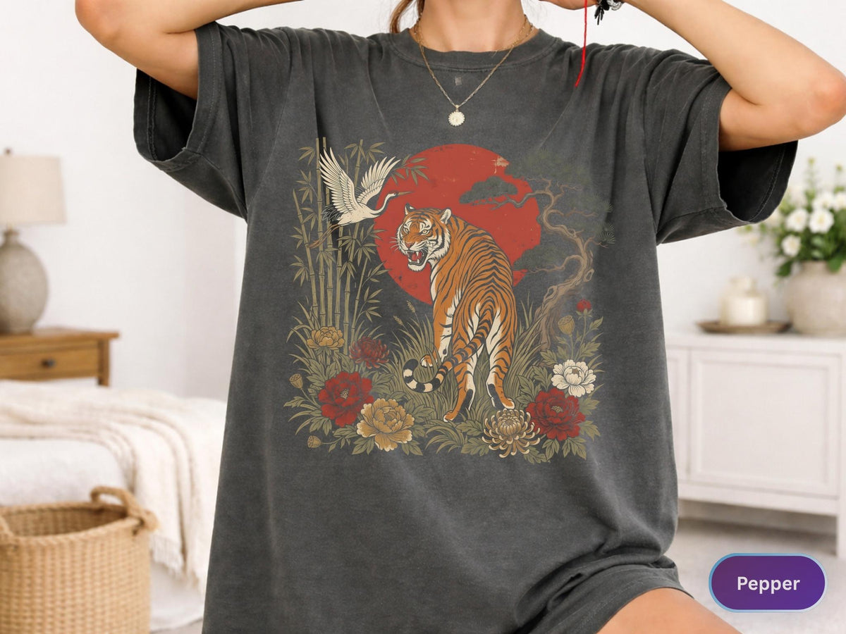 May include: Dark grey t-shirt featuring a tiger illustration with a red sun, crane, and floral elements. The design includes bamboo stalks and various flowers in shades of red, yellow, and white. The shirt has short sleeves and a relaxed fit.