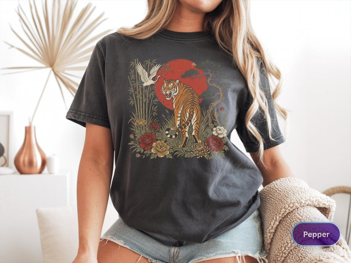 May include: Dark gray t-shirt featuring a tiger illustration with a red sun, crane, and floral elements. The design includes a tiger, bamboo, and flowers. The shirt is a comfortable, casual style.