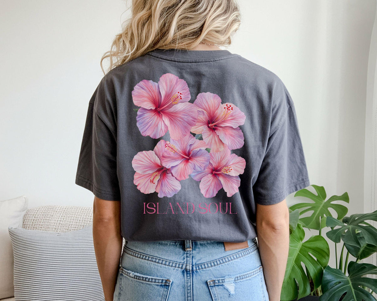 May include: Dark gray t-shirt featuring a cluster of pink hibiscus flowers on the back. The flowers have a gradient of pink and purple hues. The text "ISLAND SOUL" is printed below the flowers in pink.