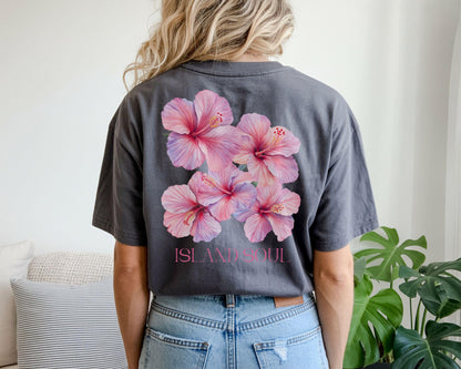 May include: Dark gray t-shirt featuring a cluster of pink hibiscus flowers on the back. The flowers have a gradient of pink and purple hues. The text "ISLAND SOUL" is printed below the flowers in pink.