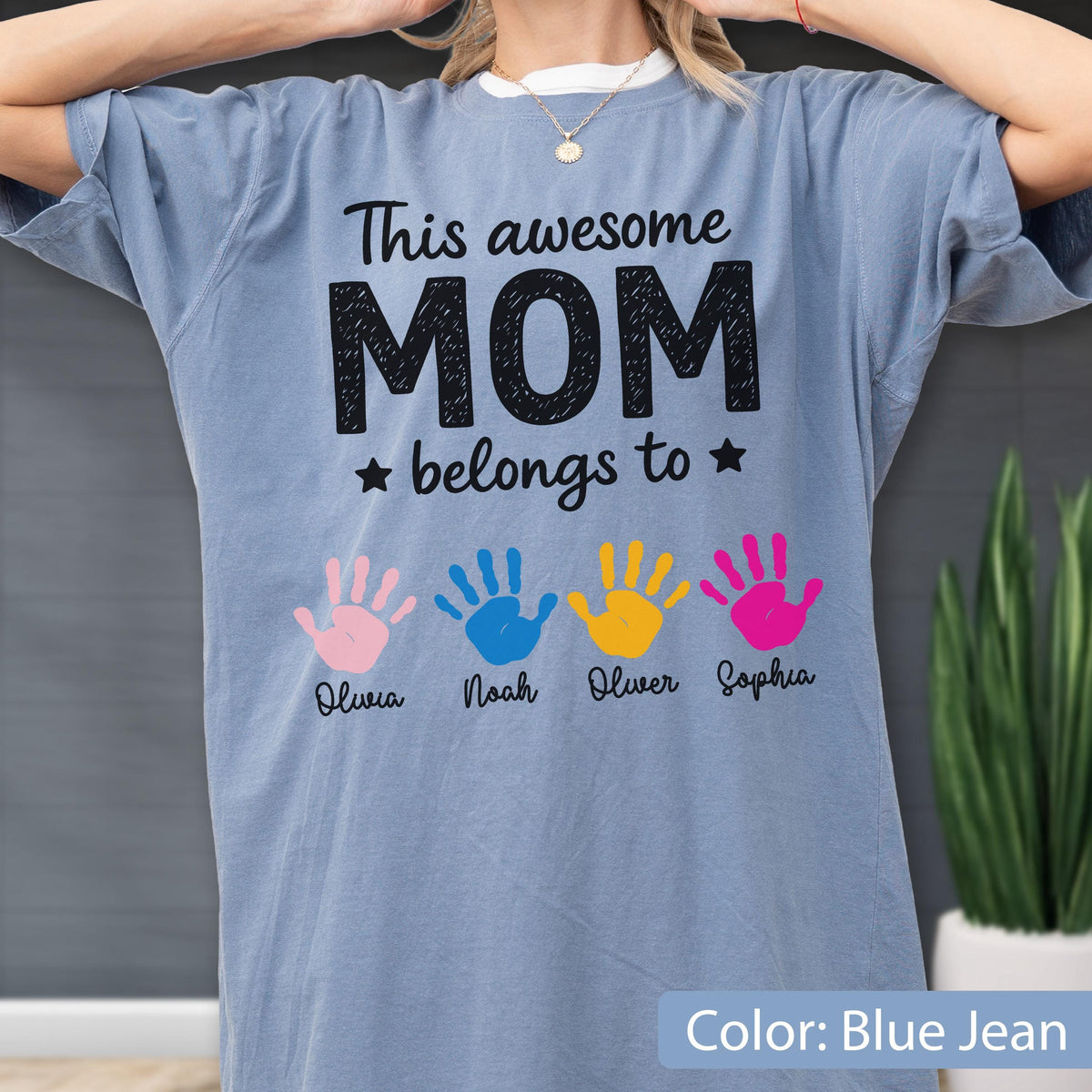 May include: Blue jean colored t-shirt with the text "This awesome MOM belongs to" and four colorful handprints. Each handprint has a name below it: Olivia, Noah, Oliver, and Sophia.