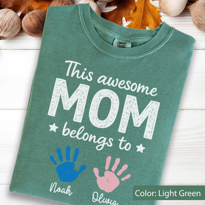 May include: Light green t-shirt with the text "This awesome MOM belongs to" and two handprints, one blue and one pink. The names "Noah" and "Olivia" are printed below the handprints. The shirt is a Comfort Colors brand.