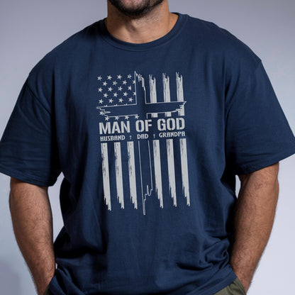 May include: Navy blue t-shirt with a white graphic design. The design features an American flag motif with the words "MAN OF GOD" and the words "HUSBAND + DAD + GRANDPA" below. The shirt is made of a soft material.