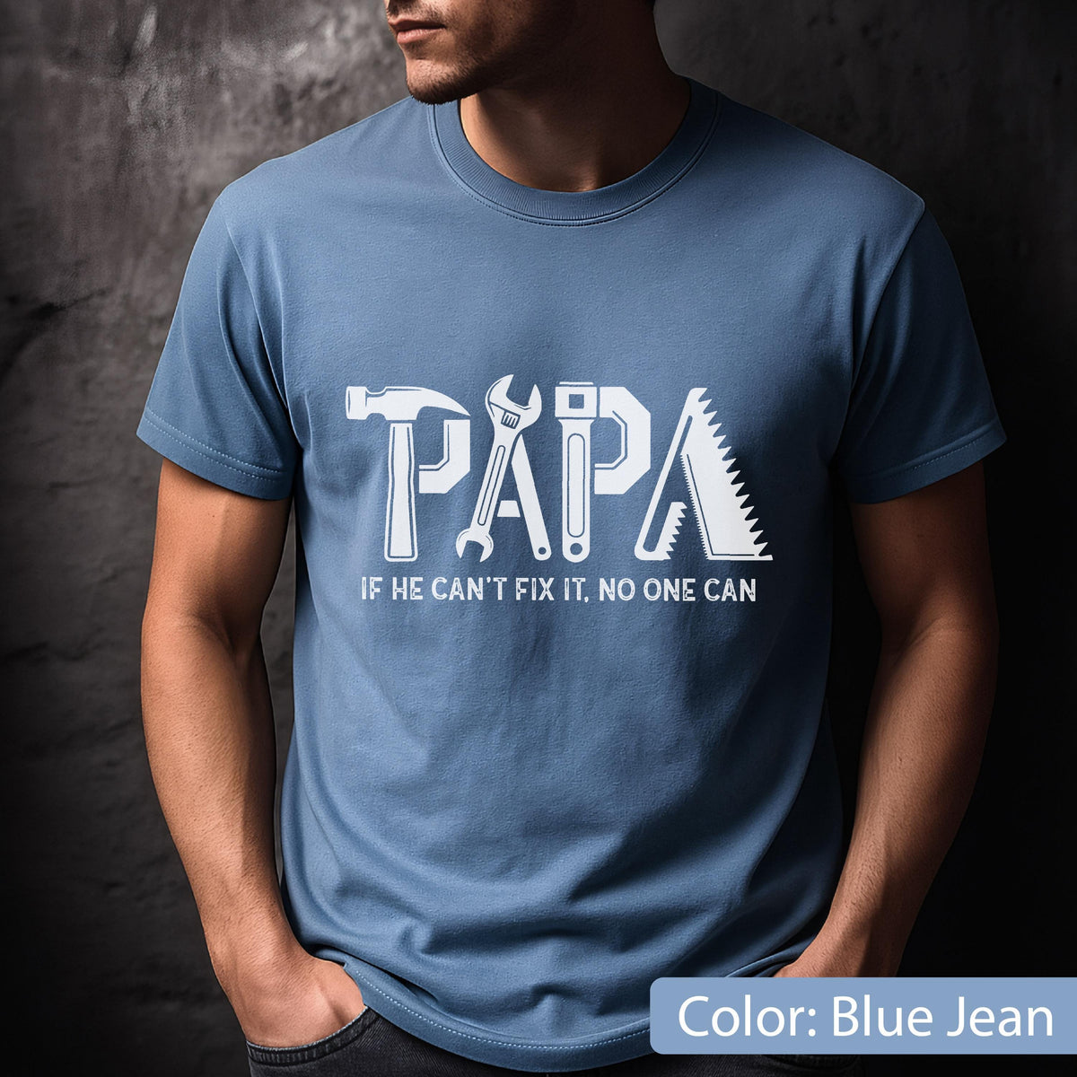 May include: Blue jean-colored t-shirt with the word "PAPA" in white, incorporating tool graphics. Below, the text reads "IF HE CAN'T FIX IT, NO ONE CAN". The shirt is a crew neck style.