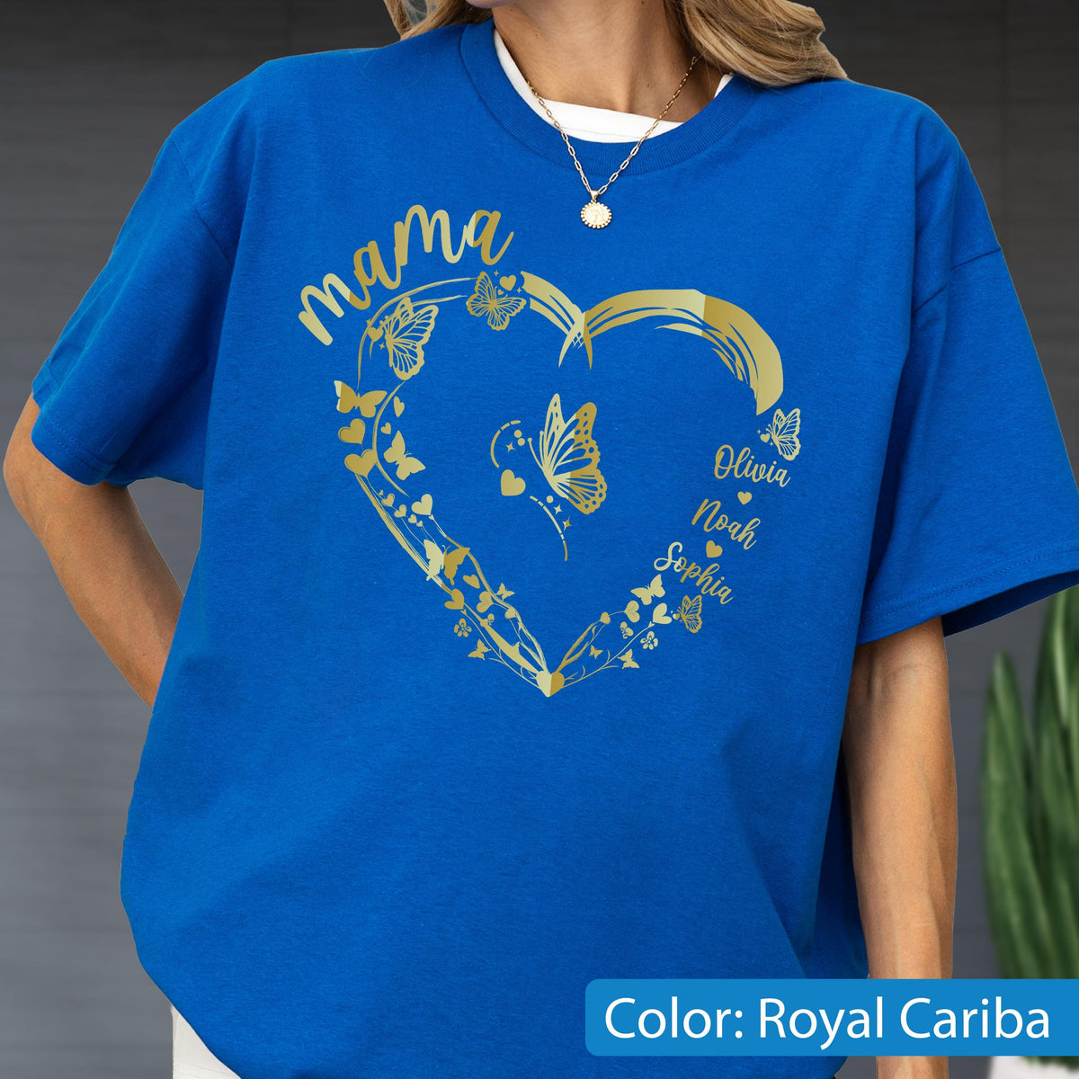 May include: Royal Cariba blue t-shirt with a gold heart design. The heart is adorned with butterflies and the word "mama". Names Olivia, Noah, and Sophia are also featured. The shirt is a solid color with a white crew neck collar.