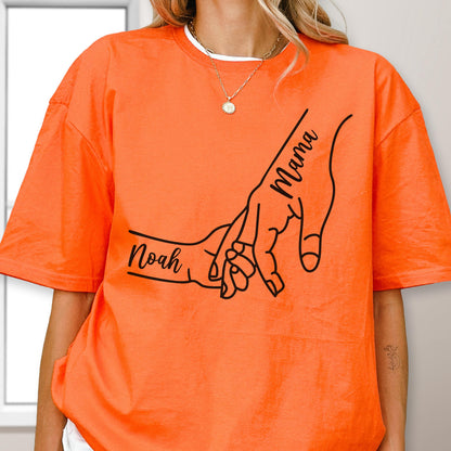 May include: Bright orange t-shirt featuring a black line drawing of two hands holding each other. One hand is labeled "Mama" and the other is labeled "Noah". The shirt has a round neckline.