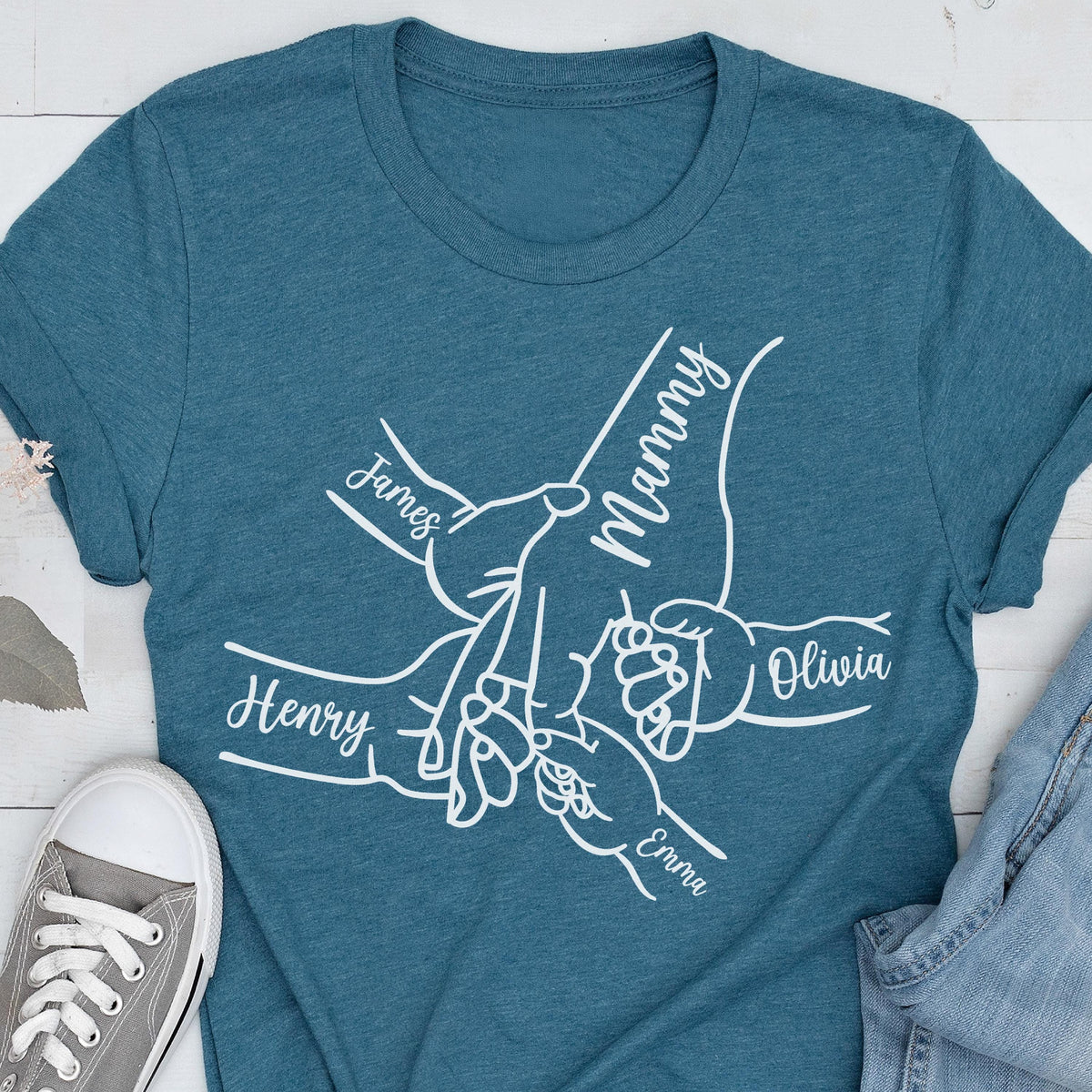 May include: Teal t-shirt with a white graphic of hands holding each other, with the names "James", "Henry", "Olivia", "Emma", and "Mammy" written on the hands. The shirt is made of a soft material.
