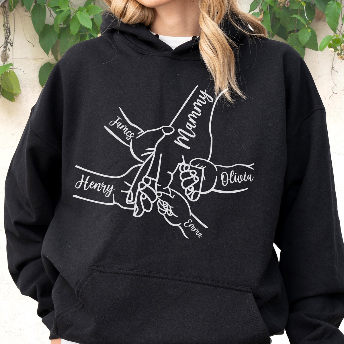 May include: Black hooded sweatshirt with a white graphic of hands holding each other. The names "James", "Henry", "Olivia", and "Emma" are written on the hands, with "Mammy" written above the hands. The sweatshirt has a front pocket and a drawstring hood.