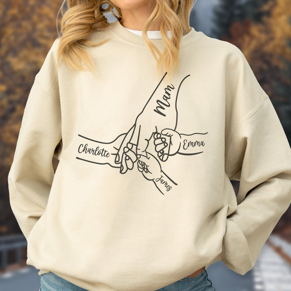 May include: Beige sweatshirt with a black line drawing of hands holding each other. The word "Mam" is written on the largest hand, with the names "Charlotte", "Emma", and "James" on the other hands.