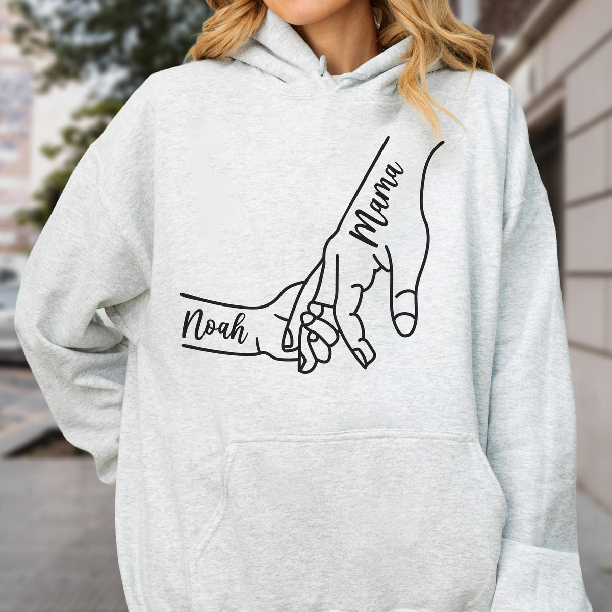May include: Light gray hoodie with a black graphic of two hands holding each other. One hand is labeled "Mama" and the other is labeled "Noah". The hoodie has a drawstring hood and a front pocket. A casual and comfortable apparel item.