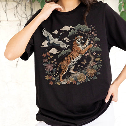 May include: Black t-shirt featuring a detailed illustration of a tiger, crane, and floral elements. The tiger is depicted in a dynamic pose, set against a backdrop of stylized clouds and foliage. The design incorporates shades of orange, brown, and green.
