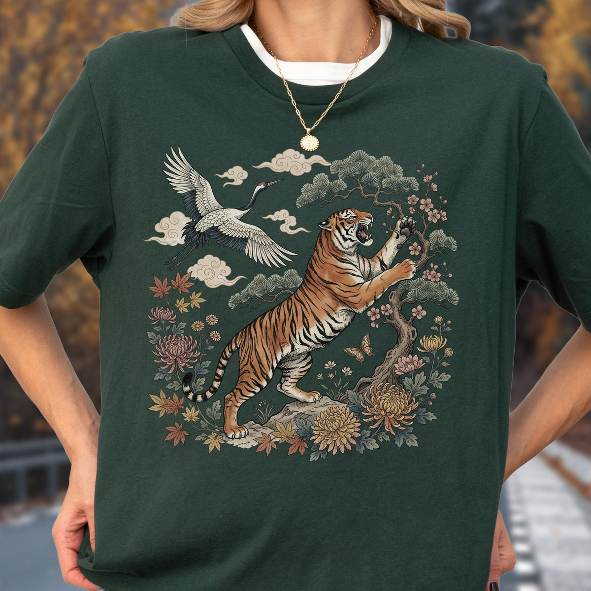 May include: Dark green t-shirt featuring a detailed illustration of a tiger, crane, and floral elements. The tiger is depicted with orange and black stripes, set against a backdrop of clouds and flowers. The shirt has a white crew neck.
