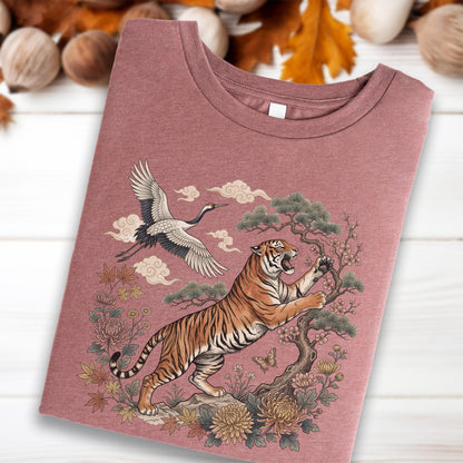 May include: A dusty rose t-shirt featuring a detailed illustration of a tiger, crane, and floral elements. The tiger is orange and black, with a crane flying above. The design includes clouds and a tree, creating an Asian-inspired theme.