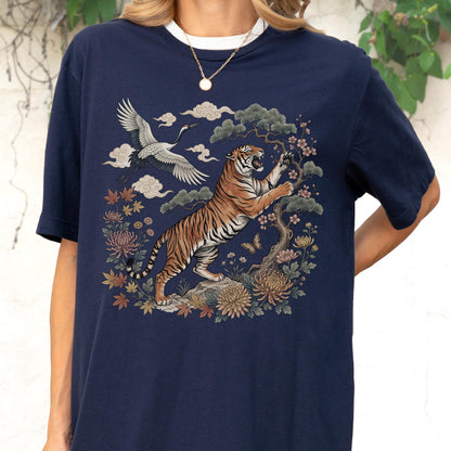 May include: Navy blue t-shirt featuring a detailed illustration of a tiger, crane, and floral elements. The design includes a tiger with orange and black stripes, a white crane, and various flowers and clouds. The shirt has a white collar.