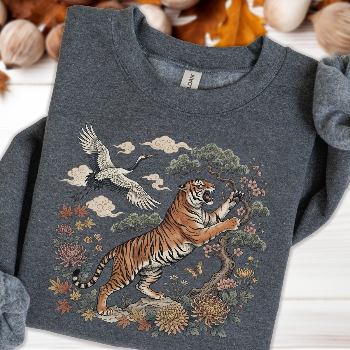 May include: Dark gray sweatshirt featuring a detailed illustration of a tiger, crane, and floral elements. The tiger is orange and black, with a tree and flowers. The crane is white and black, with clouds in the background. The design is centered on the chest.
