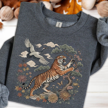 May include: Dark gray sweatshirt featuring a detailed illustration of a tiger, crane, and floral elements. The tiger is orange and black, with a tree and flowers. The crane is white and black, with clouds in the background. The design is centered on the chest.