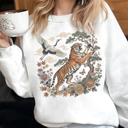 May include: White sweatshirt featuring a detailed illustration of a tiger, crane, and floral elements. The tiger is depicted climbing a tree, with a crane in flight above. The design includes a butterfly and various flowers.