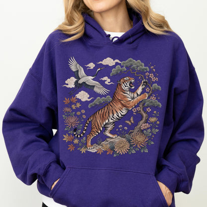 May include: A purple hoodie featuring a detailed illustration of a tiger, crane, and floral elements. The tiger is depicted with orange and black stripes, reaching towards a flowering tree. A crane flies above, with clouds and flowers completing the design.