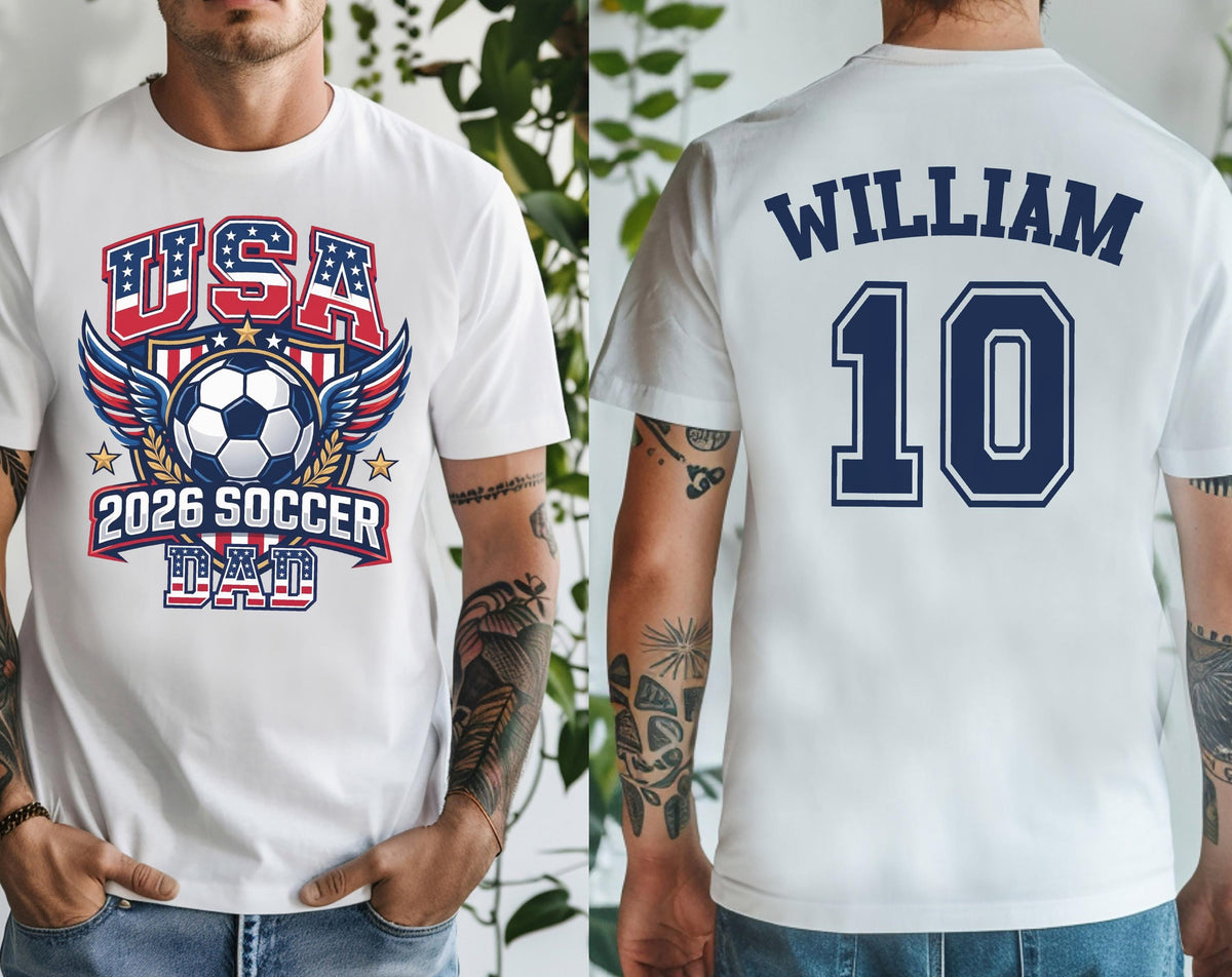 May include: White t-shirt featuring a soccer ball design with the text "USA 2026 SOCCER DAD" in red and blue. The back of the shirt displays the name "WILLIAM" above the number "10" in navy blue.