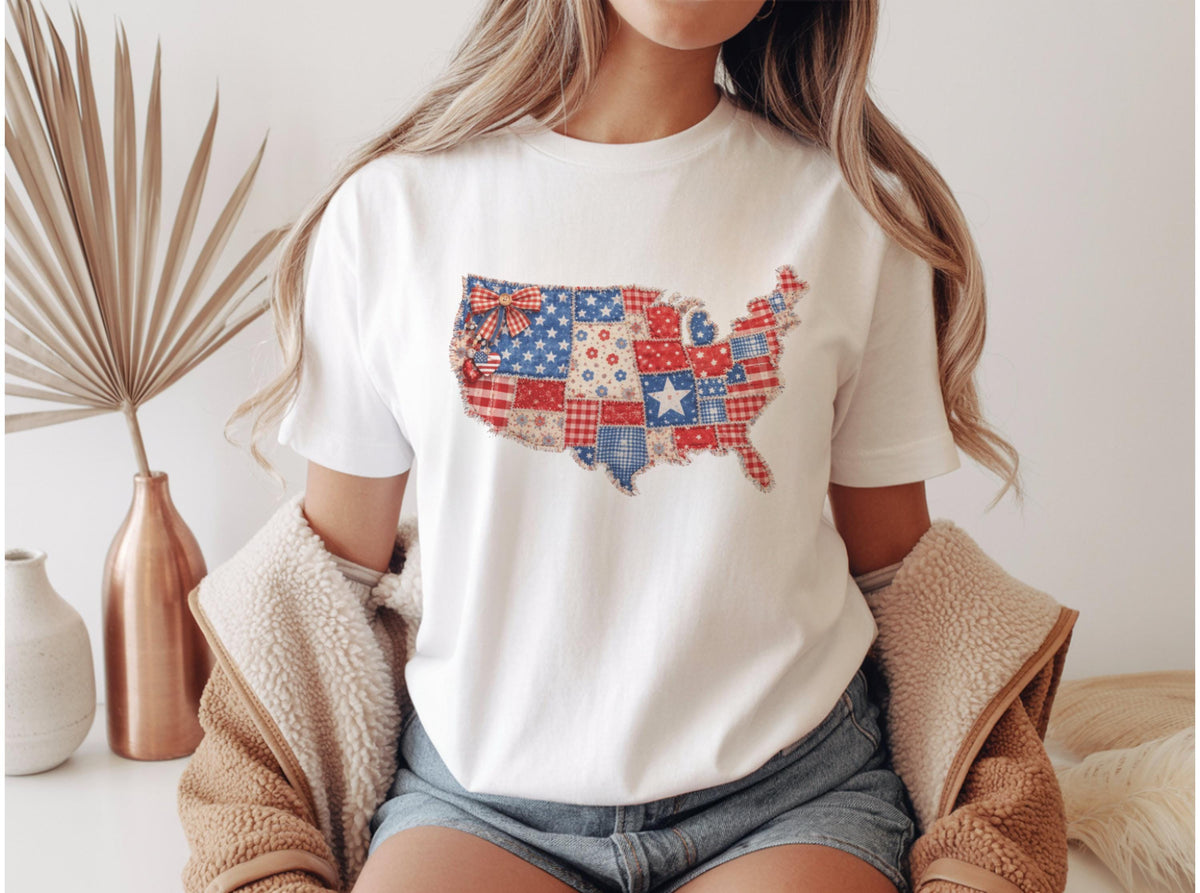 May include: White t-shirt featuring a patchwork design of the United States map in red, white, and blue. The design incorporates stars, stripes, and floral patterns. The shirt is a casual wear item.